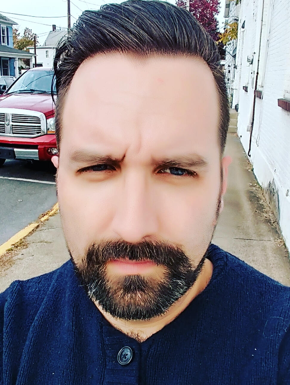 A man with glass and a white button down shirt in front of a large brick building