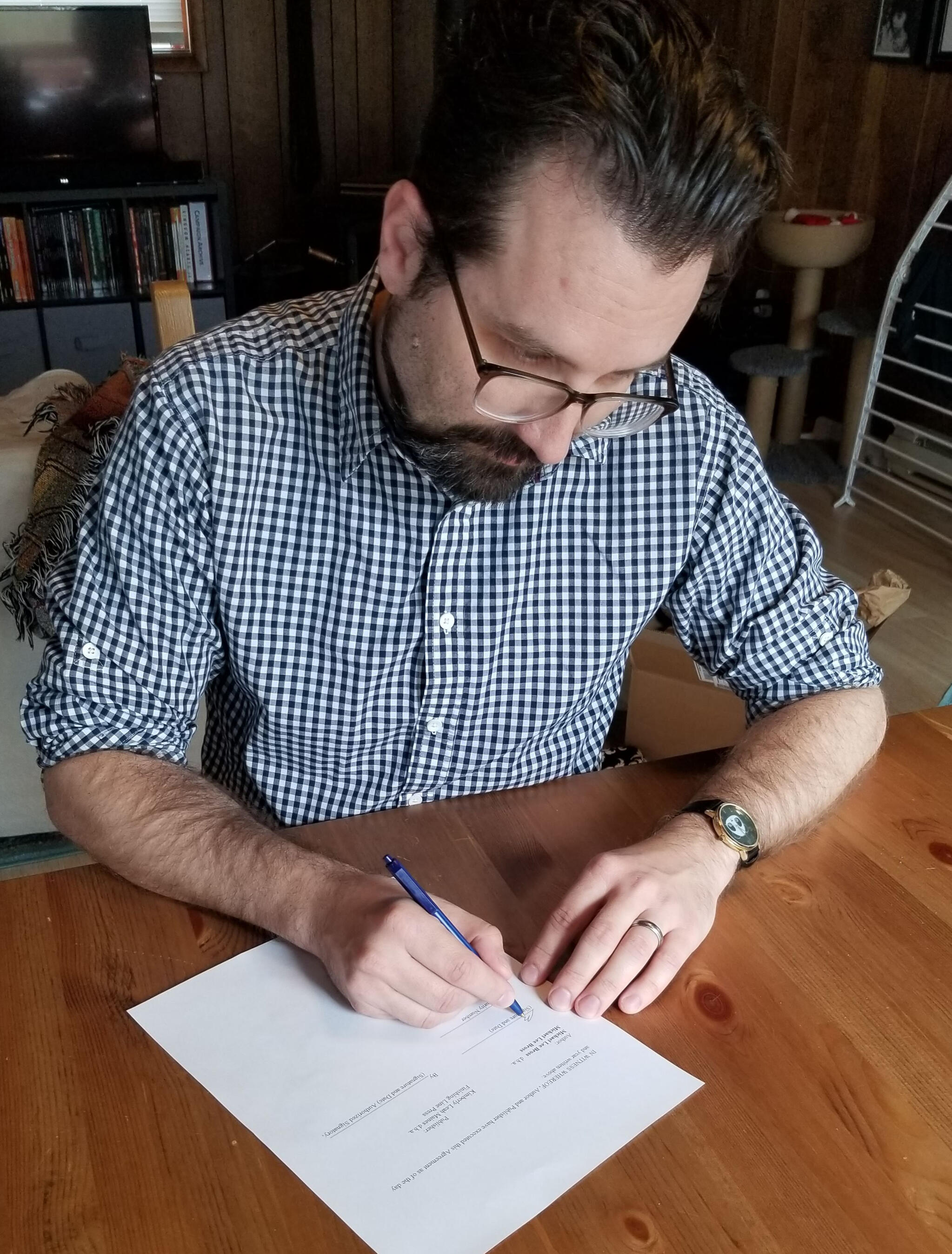 A picture of a man reading a book in front of bookshelves